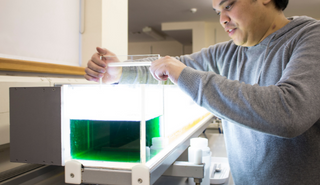 A male technician sets up a meteorology practical experiment. There is a large tub of green liquid in the foreground