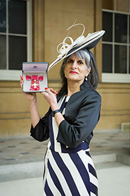 Deputy Vice-Chancellor Professor Parveen Yaqoob poses with her OBE, wearing a dark and light striped dress, dark jacket, and hat.