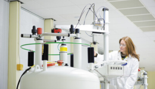 a woman in a lab coat and goggles working with a piece of scientific equipment in a lab