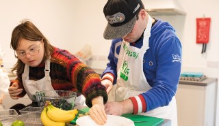A young woman and a young man, both with learning difficulties, preparing food in a kitchen