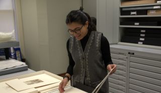 Artist in Residence Anurita Chandola looks down at a drawing in an art collection