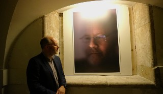 Professor Giles Harrison standing next to a portrait of himself featured in a London art exhibition