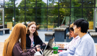 Four students, working together on laptops on a bench outside the University Library