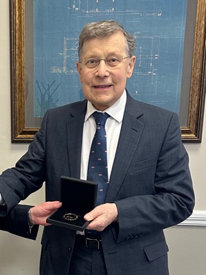 Andrew Wilbey, in a navy suit and tie, is presented with an award medal