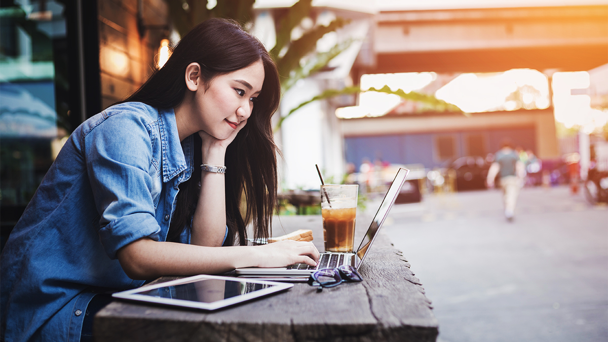 Student sitting outside a cafe with a laptop and a cup of coffee