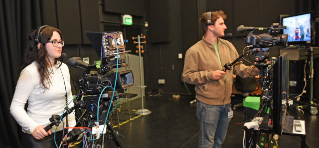 Two students behind filming cameras. 