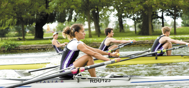 A side shot of three rowing boats alongside each other. The furthest away is a single male. The middle is a pair. The closest rower is on her own in the boat. 