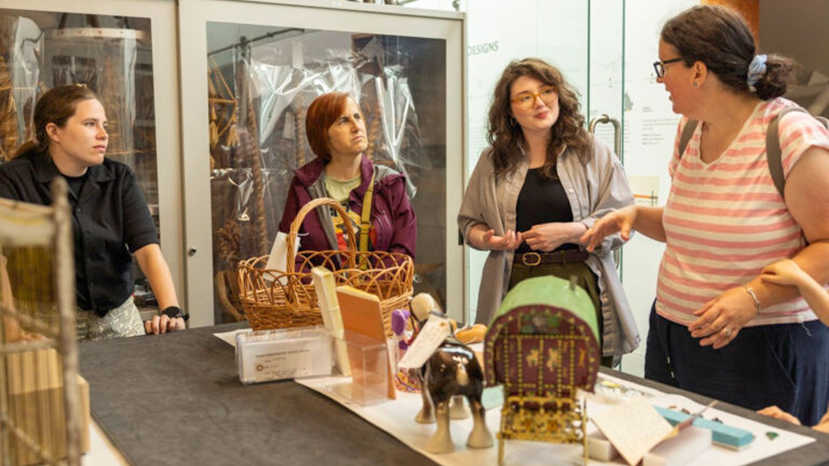 Four people standing discussing Romany artefacts on a table