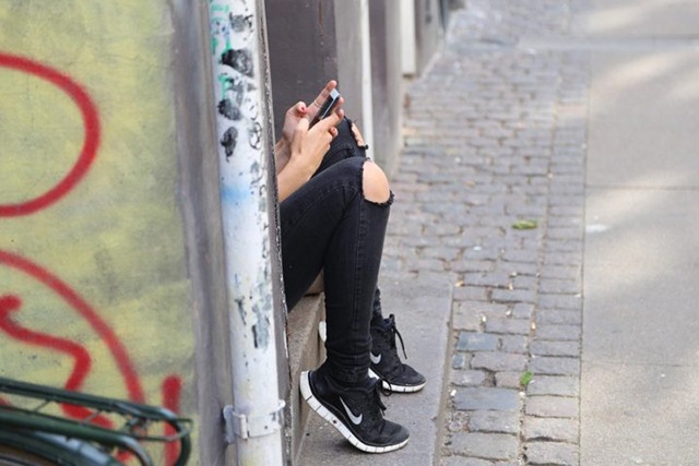 A girl holding a phone sits in a doorway, photographed in profile so only her legs and hands are visible