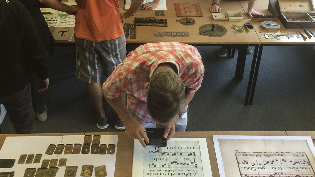 Typography student using magnifying glass to examine historic document from Department collections