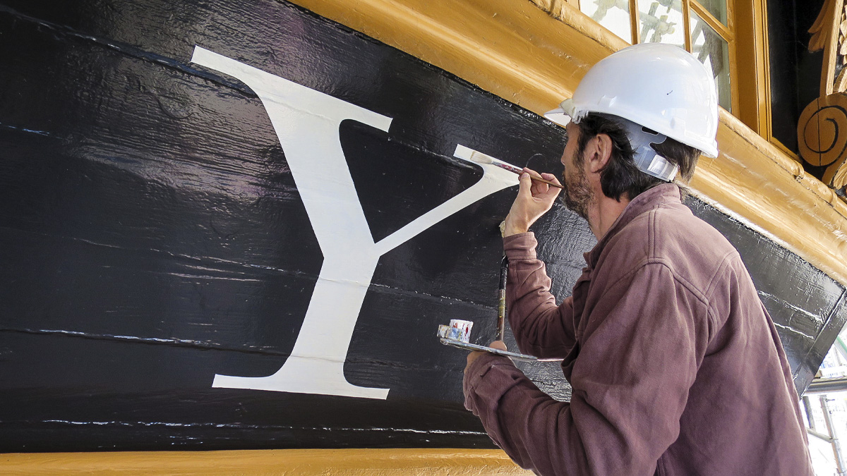 Person in hard hat painting the letter Y onto the side of a boat